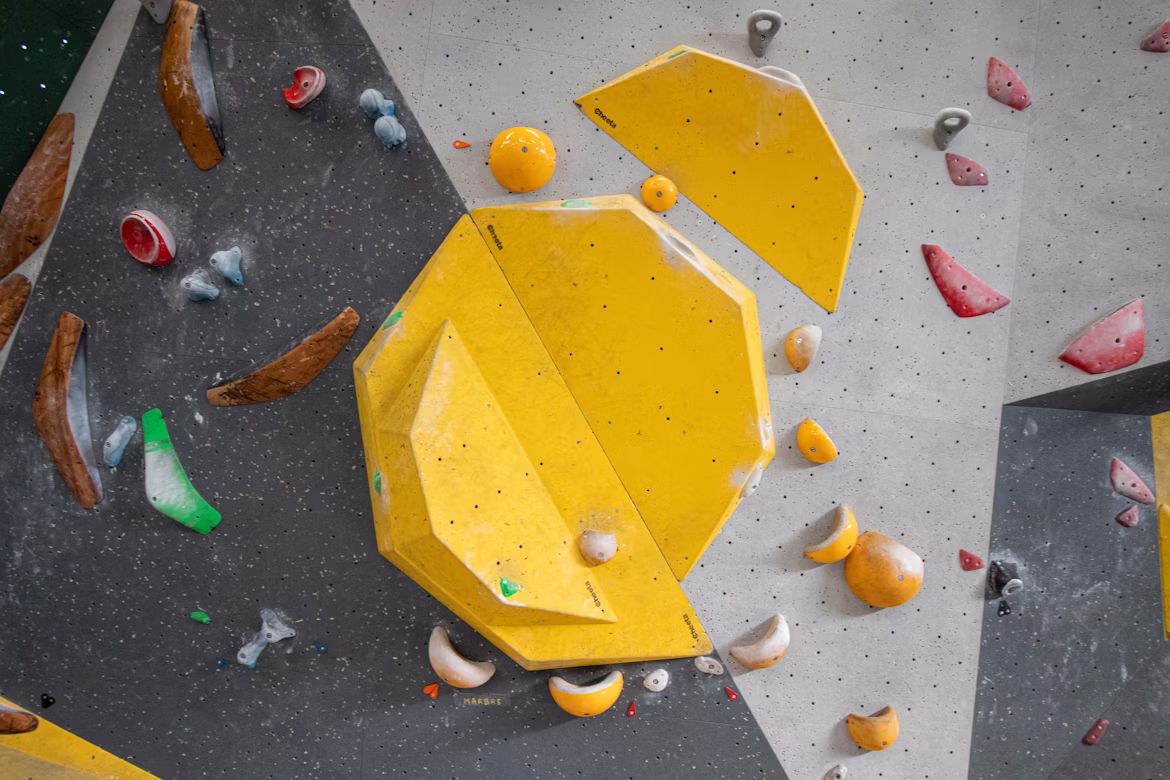 Wide indoor bouldering wall packed with bright holds above thick crash pads