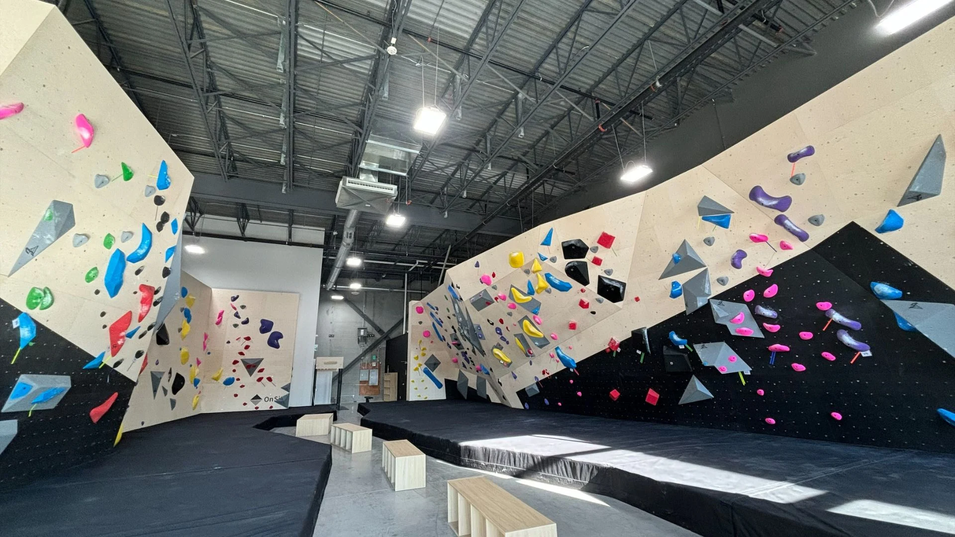 Indoor bouldering gym with angled walls, colorful holds, and padded flooring